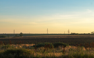 Orange sunset with blue sky in the field against the background of high voltage power lines