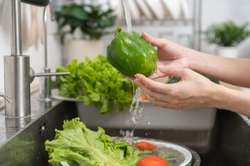 Close up hand of asian young housekeeper woman, washing sweet pepper, green paprika, vegetables with splash water in basin of water on sink in kitchen, preparing fresh salad, cooking meal. Health food