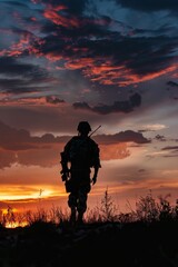 Fototapeta premium Soldier holding a rifle, silhouetted against a sunset sky, representing military service, defense, armed forces