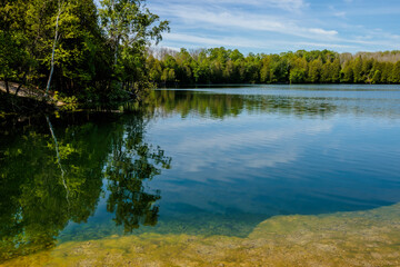 A calm lake water of Quarry Lake in early June unter the slightly streaking clouds and blue sky at Harrington Beach State Park, Belgium, Wisconsin