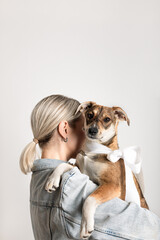 Blond woman in casual clothing standing with her back and holding young adorable dog with a white...
