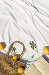 Fresh lemons, book and a wicker bag on the white sheet on the beach. Flat lay, top view, vacation concept, copy space for your text. .