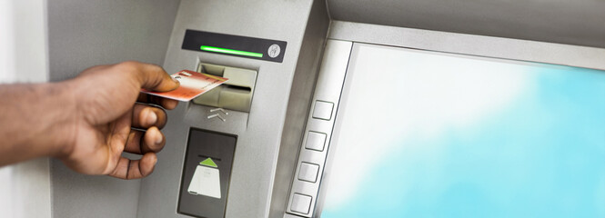 Close up of black man using ATM with gold credit card, panorama, copy space