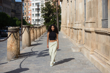 beautiful young latin woman with black eyes and dark, long curly hair walks through the centre of Seville next to the archive of the india and some 15th century stone columns. she is in Andalusia.