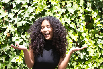 A beautiful young Latin woman with big, dark eyes, curly hair and a black shirt looks surprised and...