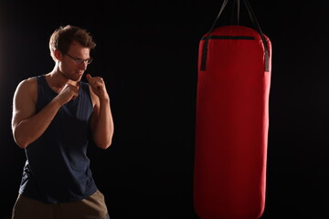 junger Mann beim Boxtraining in Boxstellung, schwarzer Hintergrund