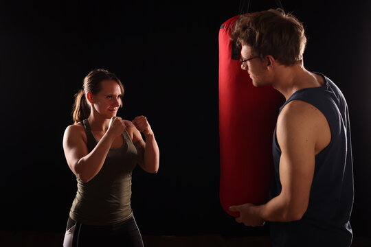 junges P&auml;rchen beim Boxtraining, er h&auml;lt den Boxsack, schwarzer Hintergrund