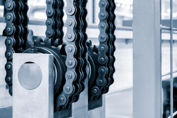 A chain is shown in a factory setting. The chain is black and silver. The chain is attached to a metal box