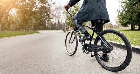Fototapeta premium Cropped of African American man in suit riding a bicycle in a park with green trees and grass in the background.