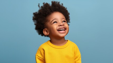 Happy child with curly hair smiling and looking up against a blue background, wearing a yellow sweater.