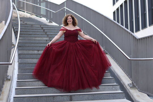 Frau im pomp&ouml;sen roten Abendkleid geht eine Treppe runter, l&auml;chelnd