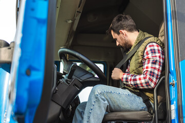 Young truck driver putting safety belt on, in his truck.