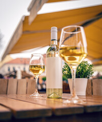 Bottle of chilled white wine and two glasses sitting on a wooden table in an outdoor restaurant