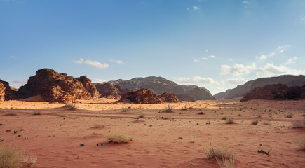 Orange red sand desert, rocky formations and mountains background, blue sky above - typical scenery...
