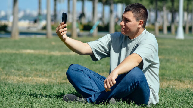 Young man sitting on the grass and talking facetime video on the phone