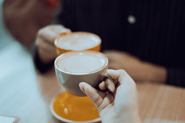 Close-up of a man and woman clinking coffee cups while talking at work.