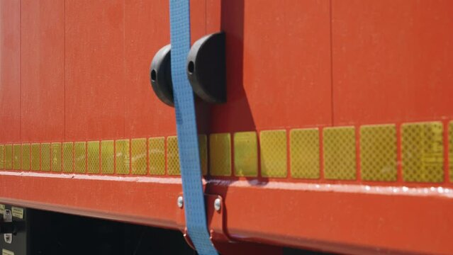 Close-up view of a blue ratchet strap securing cargo on the back of a semi-trailer.
