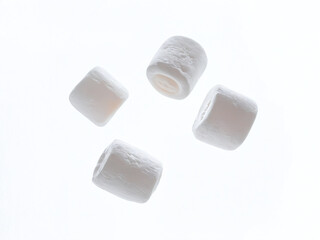 Four white marshmallows falling against a white background
