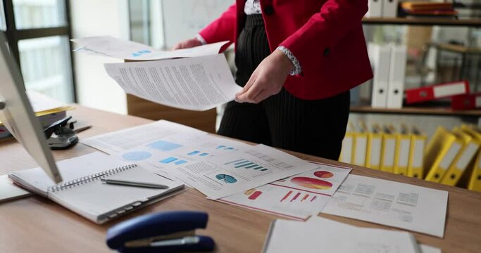 Female manager reviews infographics and puts papers on table in company office. Woman checkups actual commercial tendencies information