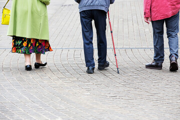 Three anonymous elderly people dressed smartly and walking along a stone paving