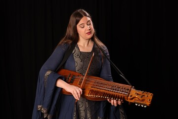 Junge Frau mit Nyckelharpa in orientalischem Kleid schaut auf Instrument vor schwarzem Hintergrund