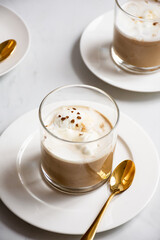 Close-up vertical of cups of coffee with cream on white plates and golden spoons