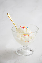 Vertical shot of bowl of vanilla ice cream with colorful sprinkles and a golden spoon