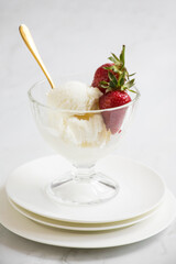 glass bowl of vanilla ice cream topped with fresh strawberries and a golden spoon on white plates