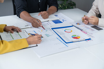 A photograph of a male and female employee's hands as they meet in an office, pens and laptops at the ready as they consult on business matters.