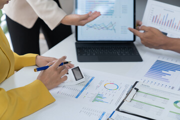 A photograph of a male and female employee's hands as they meet in an office, pens and laptops at the ready as they consult on business matters.