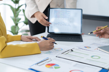 A photograph of a male and female employee's hands as they meet in an office, pens and laptops at the ready as they consult on business matters.