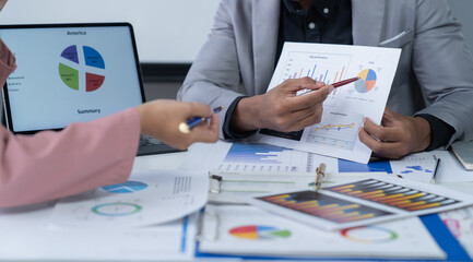 A photograph of a male and female employee's hands as they meet in an office, pens and laptops at the ready as they consult on business matters.