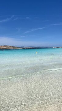 Vertical video. White sand beach on a narrow strip of land on Formentera. Blue famous beach with people relaxing on vacation in the mediterranean sea with luxury vessels and boats. Turquoise sea.