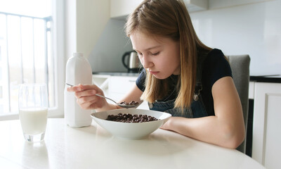Girl Having Brown Chocolate Balls Cereal For Breakfast In The Kitchen In The Morning