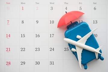 Airplane, suitcase and umbrella on white calendar background. Travel holiday or annual leave travel...