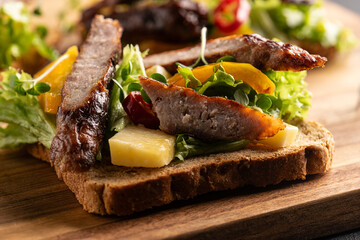Tasty homemade sndwiches with grilled vegetables and sausages and fresh juicy salad leaves on the serving board close up. 