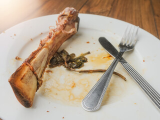 A plate of food with a fork and knife on it. The plate has a piece of meat bone on it and a napkin. End of fine dinner with high quality steak on the bone. Premium product.