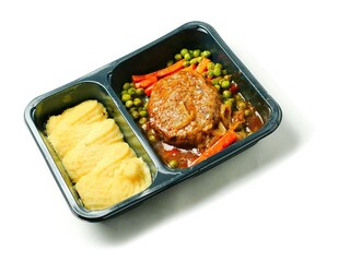 A meal consisting of burger, mashed potatoes and vegetables in black plastic tray on white background. Simple classic dish for take away. Office lunch.