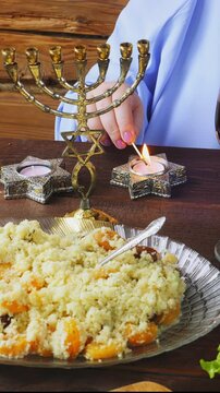 A Jewish woman in blue lights candles at the Pesach Seder table