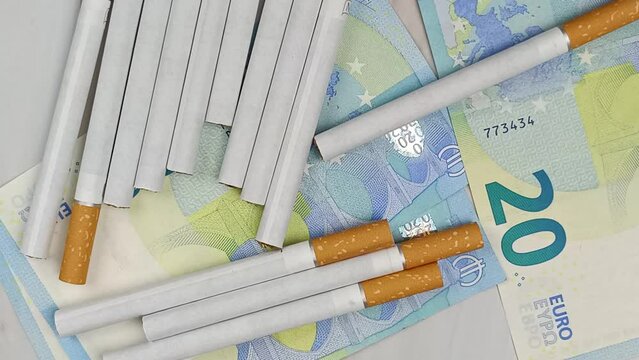 plusieurs cigarettes et billets de vingt euros, en gros plan, vue du dessus.