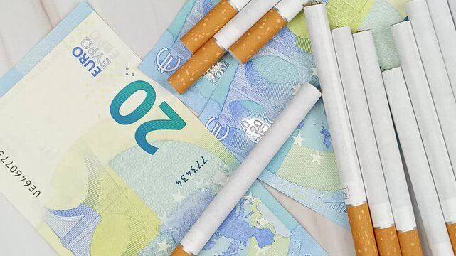 plusieurs cigarettes et billets de vingt euros, en gros plan, vue du dessus.