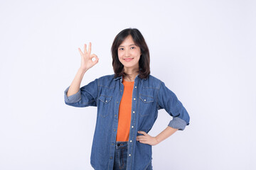 Asian woman wearing orange t shirt and denim jean is posing with an okay gesture on a white background.