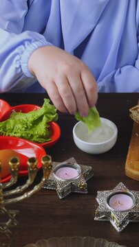 A Jewish woman in blue at a laid Pesach Seder table dips karpas in salt water