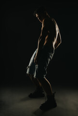 Contemporary male dancer striking a dynamic pose in dark lighting, wearing denim shorts and boots, showcasing strength and artistic expression.