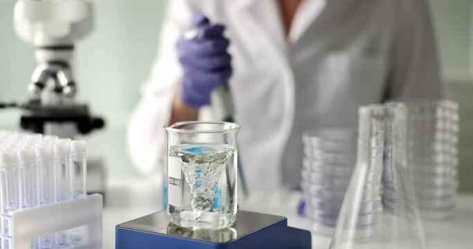 Laboratory assistant prepares water in flask for detailed investigation. Woman doing examination of liquid in glassware making swirl slow motion