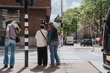 Lesbian couple in Amsterdam waiting at a pedestrian crossing. A sunny day in the city showcasing...