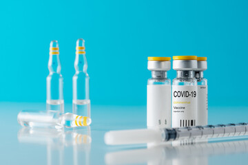 Coronavirus vaccine vial glass with a syringe on blue background.