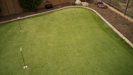 An artificial turf putting green with a desert landscaped boarder in a residential backyard.