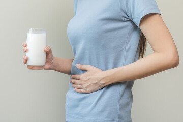 Pain, suffering asian young woman having a stomachache, abdominal pain or digestive, hand in holding belly after drink glass of milk. Lactose intolerance, allergy from dairy food, health care problem.