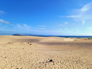 Landscape in desert sand dunes and volcanoes background with white clouds and blue sky in Fuerteventura. View on white sand desert, mountains at the horizon and blue sky.
